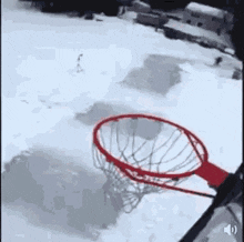 a person is playing basketball in the snow and the ball is going through the hoop .