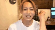 a young man in a white t-shirt is smiling in front of a computer screen