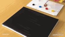 a black book is sitting on a wooden table next to a palette of paints made in animatica