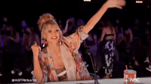 a woman sitting in front of a crowd with her arms in the air and a coca cola can in front of her