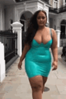 a woman in a blue dress is walking down a sidewalk in front of a building .