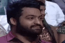 a man with a beard is sitting in a crowd of people and making a face .