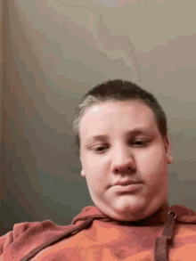 a young boy with a shaved head is wearing an orange sweatshirt