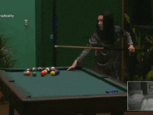 a woman is playing pool in front of a green wall with the word reality at the top