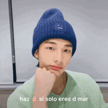 a young man wearing a blue beanie and a green sweater is making a peace sign