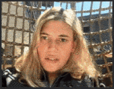 a woman with long blonde hair is sitting in front of a rope fence