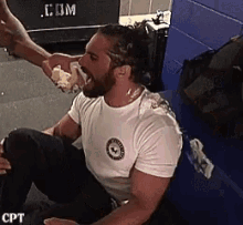 a man in a white shirt is sitting on the floor and eating a piece of food .