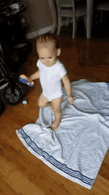 a baby in a white bodysuit is standing on a blanket