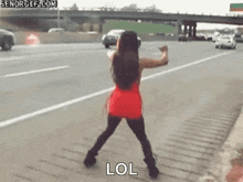 a girl in a red dress is dancing on the side of the road .