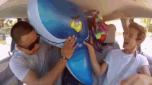 two men are playing with a large inflatable shark in the back seat of a car .