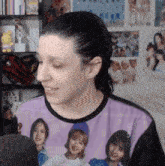 a woman wearing a purple shirt with a picture of a group of girls on it is talking into a microphone .