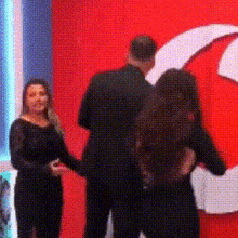 a man and two women are standing in front of a red wall with the letter g on it