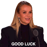 a woman in a black jacket stands in front of a microphone with the words good luck below her