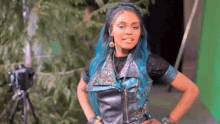 a woman with blue hair is standing in front of a green screen and a camera .