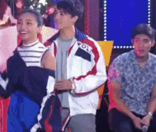 a man and a woman are standing next to each other on a stage . the man is wearing a polo jacket .