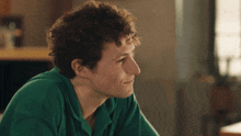a young man with curly hair is wearing a green shirt and smiling