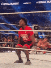 a man in a red shirt is squatting in a wrestling ring