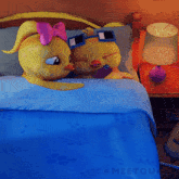 a couple of cartoon characters laying on a bed with a blue blanket and a lamp