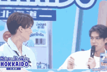 two men are talking in front of a hokkaido sign