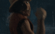 a man in a hat and vest is standing next to another man in a dark room .