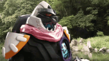 a robot with a pink scarf around his neck is standing next to a river
