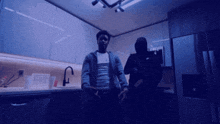 a man in a mask stands next to a man in a blue jacket in a kitchen