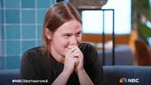 a woman covering her mouth with her hands and a nbc logo in the background