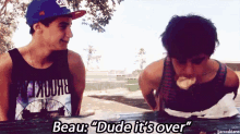 two young men are sitting at a picnic table and one of them is wearing a tank top that says " beau "