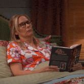 a woman is laying on a couch reading a book called the queen 's dilemma