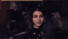 a woman wearing headphones is sitting in front of a microphone and looking at the camera .