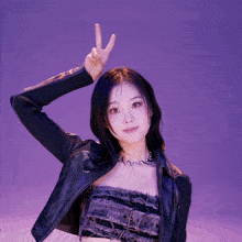 a woman wearing a leather jacket and a necklace giving the peace sign