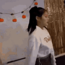 a woman in a white shirt is standing in a room with pumpkins hanging from the ceiling .