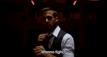 a man in a suit and tie is standing in a dark room and says wanna fight .