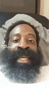 a man with a beard wearing a hat is laying on a bed .