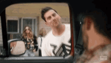 a man in a white shirt is looking out the window of a car and making a funny face .