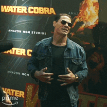 a man wearing sunglasses stands in front of a poster for water cobra
