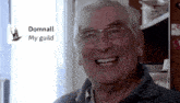 an elderly man with glasses is smiling in front of a sign that says dommall my guild