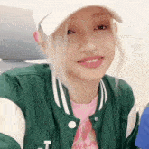 a young woman wearing a green jacket and a white hat is smiling .