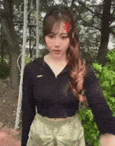 a girl with a red heart on her forehead is standing in front of a tree .