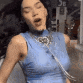 a woman wearing a blue tank top and a necklace is singing .