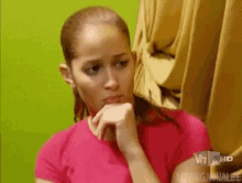 a woman in a pink shirt is sitting in front of a green wall .