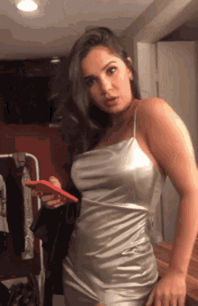 a woman in a silver dress is holding a red cell phone