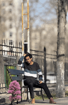 a young man sits on a park bench with his hand on his head