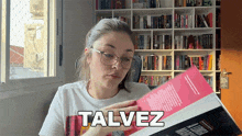 a woman wearing glasses is reading a book and the word talvez is above her head