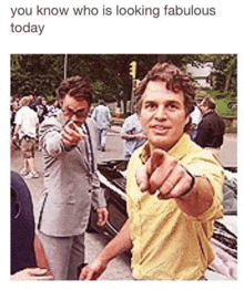 a man in a suit and yellow shirt is pointing at the camera with his finger .