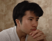 a young man with his hand on his chin looks to the side