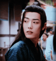 a young man with long black hair is wearing a blue shirt