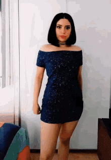 a woman in a blue dress stands in front of a white wall