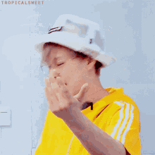 a person wearing a yellow shirt and a white hat with the word tropicalsweet written on the bottom