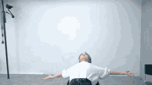 a person with their arms outstretched is sitting in front of a white wall
